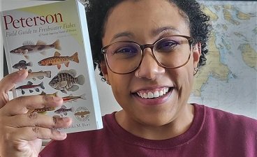 smiling woman with glasses holding a book on fishes