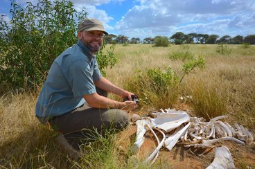 smiling man in field next to animal bones