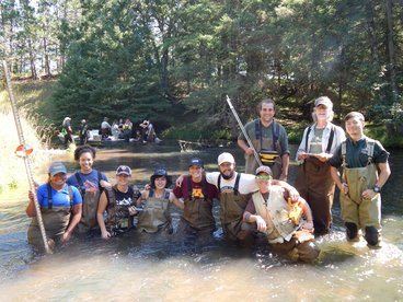 ten people wearing waders posing in river